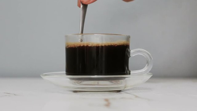 Hand of man using coffee spoon to mix black and hot coffee into a clear cup of coffee Close up shot