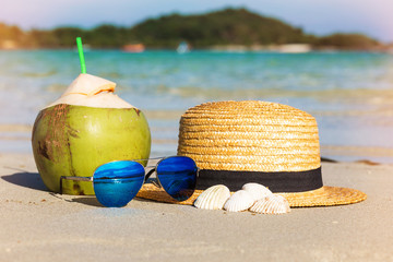 Photo concept of summer vacation, coconut, sunglasses, sea shells, straw hat. Sea beach in the background tropical island