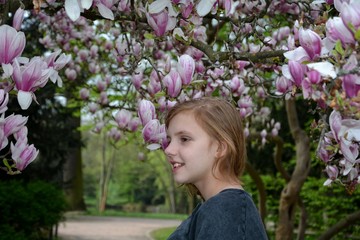 Fototapeta premium Mädchen steht unter blühenden Magnolienbäumen ( Magnoliaceae ) und lacht zur Seite
