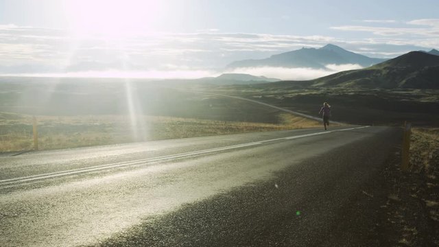 woman running up road in Iceland with mountains in background