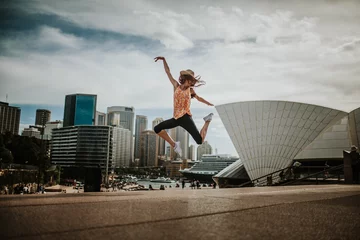  Gelukkige vrouw die in de lucht springt in Sydney, met het stadsbeeld op de achtergrond. Australië. © daviles