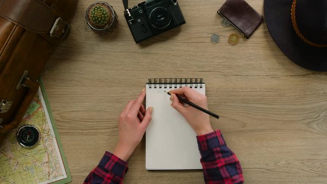 Young woman make some notes in note book on wood background. Woman hands make travel list for the future trip. Top view.