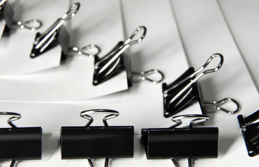 Black binder clips in a row clamping the paper close up white background