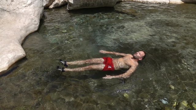 Man swimming, floating in natural pool, super slow motion 240fps
