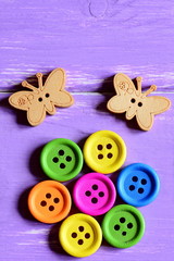 Bright wooden round buttons laid out in the shape of a flower on a green paper sheet, wooden butterfly buttons. Wooden background. Funny summer card. Closeup. Top view. Vertical photo