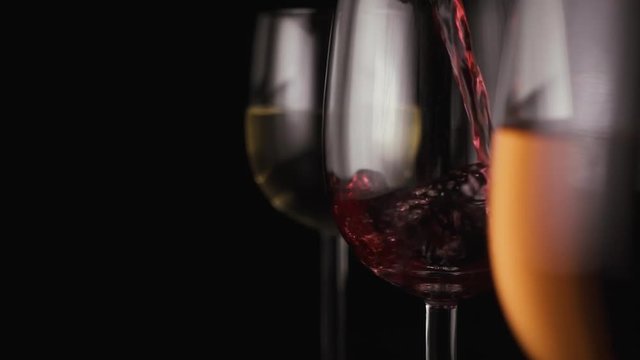 Red wine is poured into one of the three glasses. Black background. Slow motion