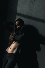Sensual young fitness woman in sportswear posing and leaning on black