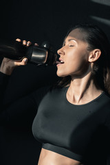 Young fitness woman in sportswear drinking water with closed eyes