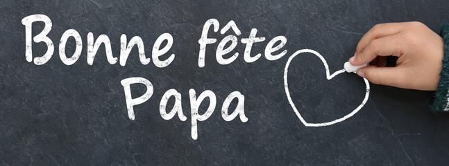 Main d'enfant écrivant bonne fête papa et dessinant un coeur à la craie sur une ardoise