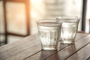 Glass water on wooden table with poor light background.