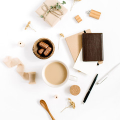 Blogger or freelancer workspace with coffee mug, notebook, sweets and accessories on white background. Flat lay, top view minimalistic brown styled home office desk. Brown styled composition
