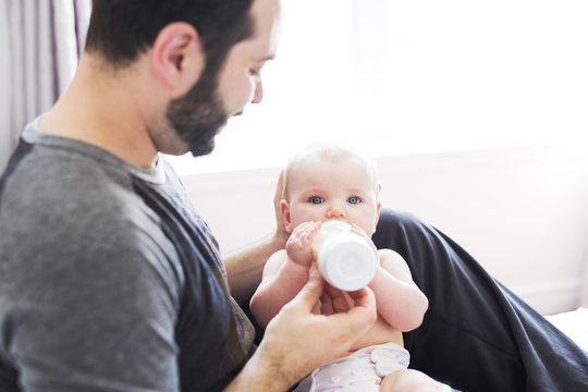 Happy Man Feeding Milk To Baby Girl At Home