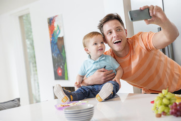 father and toddler son taking selfie in kitchen at home