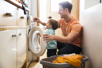 Father and toddler son doing laundry at home - obrazy, fototapety, plakaty