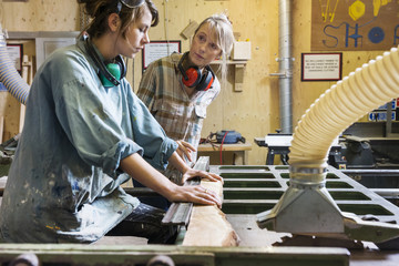 Two women talking and using machinery in a wood workshop