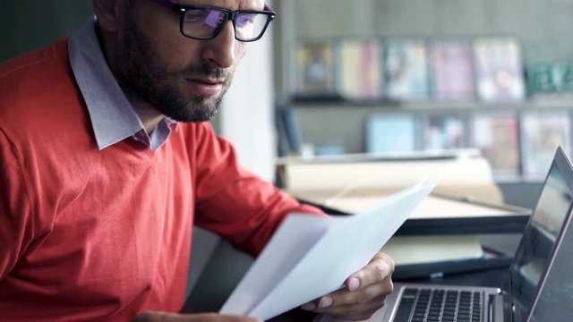 Sad, overwhelmed businessman with laptop and documents sitting by desk, 4K
