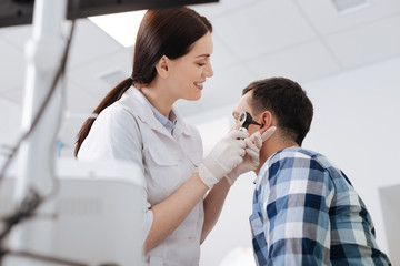 Profile photo of otolaryngologist holding otoscope near ear of patient