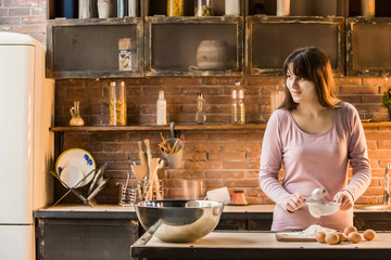 A young brunette sifts through a sieve on a kitchen table. On the table lay eggs.