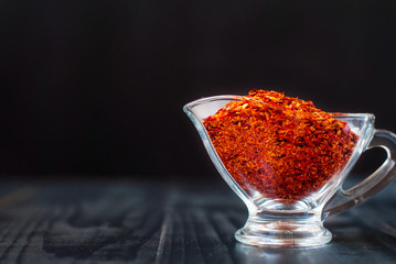 Chile pieces in a glass jar. Red ground chili on a dark background.