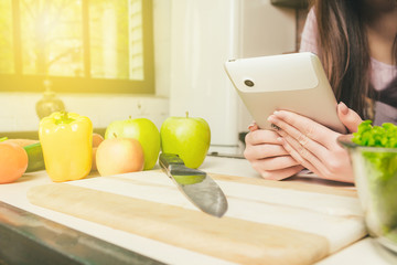 Woman Using Digital Tablet With Vegetable On Countertop In Kitchen.Close-up hands with tablet and vegetables on table