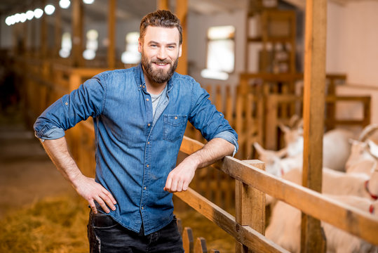 Portrait of a handsome farmer standing in the barn with goats. Natural milk production and farming