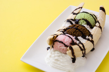 Banana split ice cream dessert with chocolate syrup on yellow background
