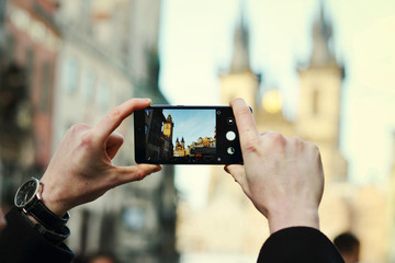 Close up of a tourist's hands holding phone and taking photo of building in centre of Prague