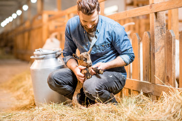 Handsome farmer taking care of cute goat baby at the barn