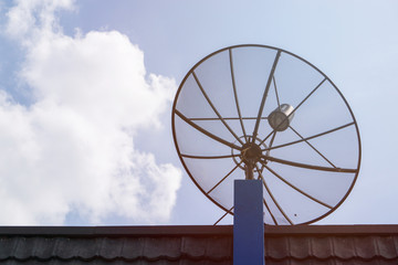 Black satellite dish or TV antennas mounted on the roof of house with blue sky cloudy background.