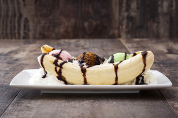 Banana split ice cream dessert with chocolate syrup on wooden background  