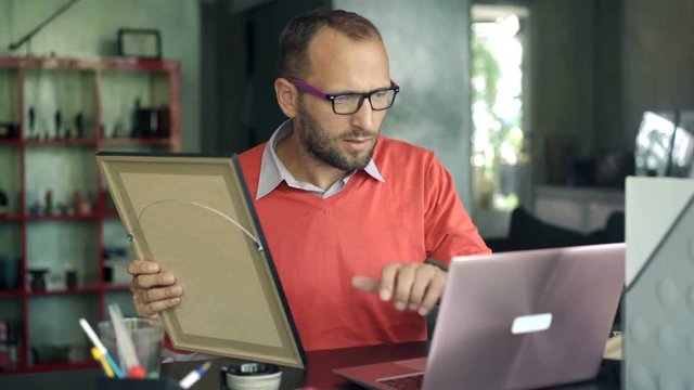 Young art curator looking and painting and checking something on laptop, 4K

