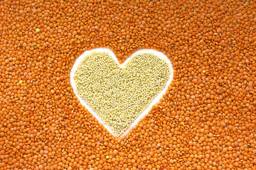 Heart shape made of mixed yellow wheat grains and orange red lentils on table surface, top view. Dry cooking ingredients for a healthy food.