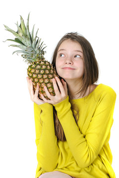 Charming young girl holding a large ripe pineapple and looking up..