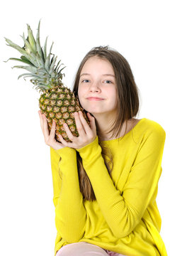 Charming young girl holds a large ripe pineapple in her hands..