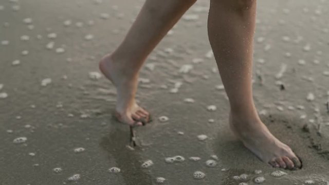 Female feet walk on wet sand on the coast of the sea
