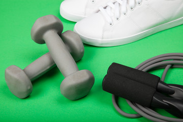 Sport shoes, dumbbells and skipping rope on green background. Fitness, sport and healthy lifestyle concept.