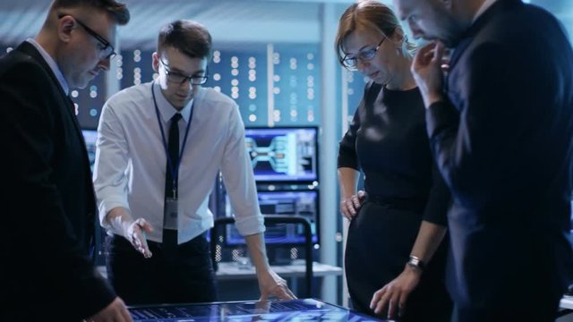 Team of Government Agents Tracking Fugitive with Help of Touchscreen Interactive Table in Big Monitoring Room Full of Computers with Animated Screens.Shot on RED EPIC-W 8K Helium Cinema Camera.