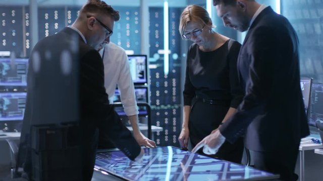 Team of Government Agents Tracking Fugitive with Help of Touchscreen Interactive Table in Big Monitoring Room Full of Computers with Animated Screens. Shot on RED EPIC-W 8K Helium Cinema Camera.