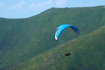 Paragliding in the blue sunny sky. One paraglider fly in summer sunny day in the clouds. Carpathians, Ukraine. Paragliding over the mountain valley.