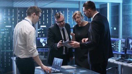  Team of Government Officials Have Constructive Discussion in Monitoring Room. Man Holds Tablet, Laptop is Seen on the Table. Computers have Animated Screens.