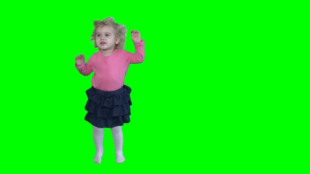 Adorable girl with blond curly hair dancing and jumping isolated on green