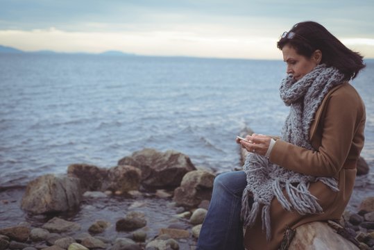 Woman using smartphone while sitting by the sea