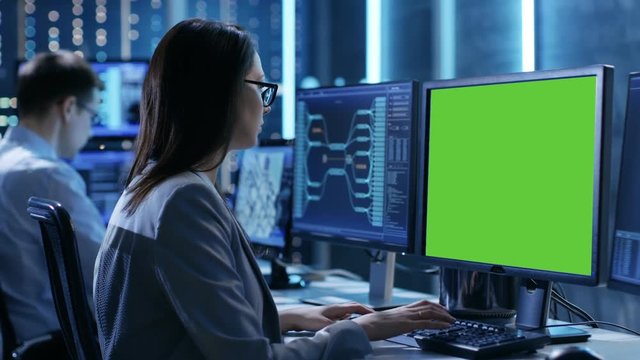 Female Controller/ Operator Working at His Workstation with Multiple Displays (Green Screen Mock-up). Possible Power Plant/ Airport Dispatcher/ Dam Worker/ Government Surveillance/ Space Program. 