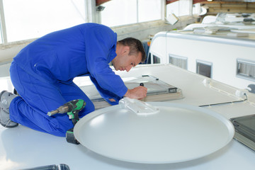 Mechanic fitting satellite dish to roof of camper van © auremar