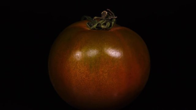 Close up of pink and green tomato with stem, rotating on black background to the right, contra-clockwise. Amazing texture of fresh vegetable in 4k, 3840x2160, clip.
