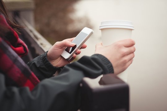 Cropped woman using mobile phone while holding disposable cup