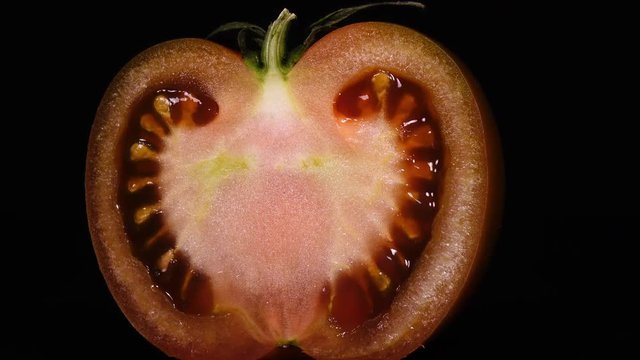 Excellent close up of slit pink tomato with stem, rotating on black background to the right, contra-clockwise. Amazing texture of fresh vegetable in 4k, 3840x2160, clip.
