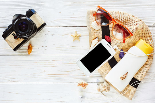 summer travel vacation flat lay concept. photo camera and hat sunscreen phone with empty screen and sunglasses on white wooden background, top view. hello summer. wanderlust. space for text