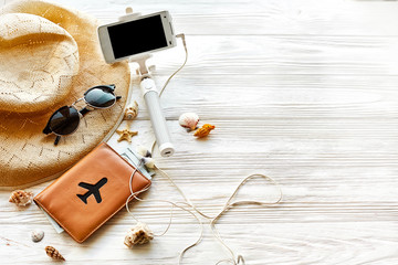 Fototapeta na wymiar summer travel vacation concept, space for text. selfie stick phone camera passport money plane hat and sunglasses on white wooden background. hello summer. wanderlust. save moments