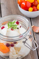 Merinated cherry tomatoes and saurkraut in a glass jar on a wooden table. Pickled vegetables